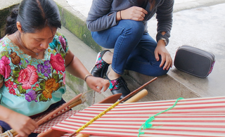 A woman weaving and a person sitting next to her on the ground